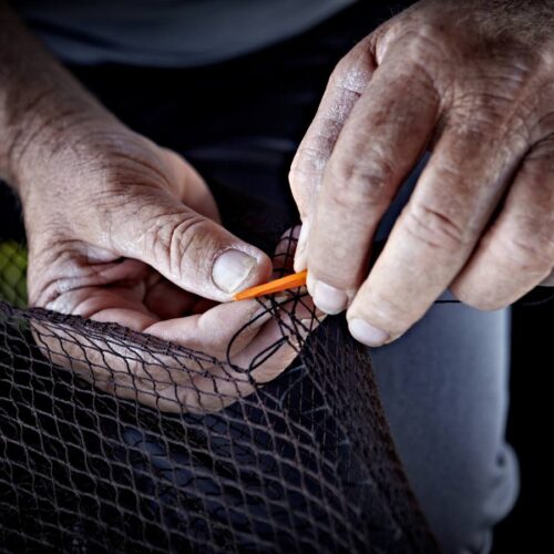 Crop from above view of man holding fishing net in hands and cutting with knife